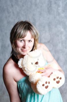 A beautiful and sexy 20-25 years blond girl with teddy bear  in dress on grey background