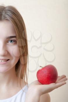 Beautiful blonde woman holding a red apple in left hand - health concept. Pretty smile deep blue eyes half of the face