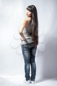 back view of standing young beautiful Asian woman in tank top and jeans. Teen watching. Rear view. Backside view of person. Shot over white background.