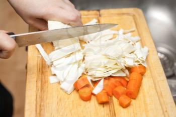 Woman's hands cutting carrot, near fresh vegetables.