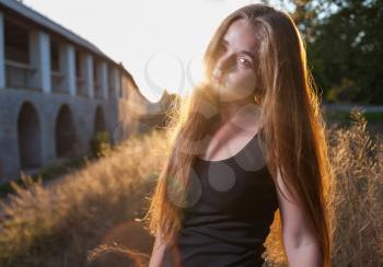 Young Woman In The Autumn Park at Sunset. Backlit. Picture of beautiful female over sunset, closeup portrait of romantic girl, attractive blond woman enjoying autumn golden sunlight, pretty young lady