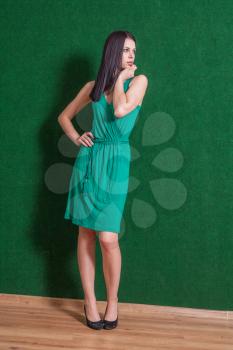 brunette weared green dress standing indoors, against green wall