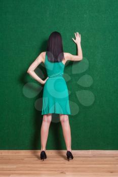brunette gesturing against green wall. Hand up.