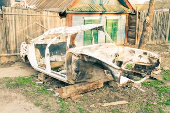 Rusty car body against old wooden houses in Russia