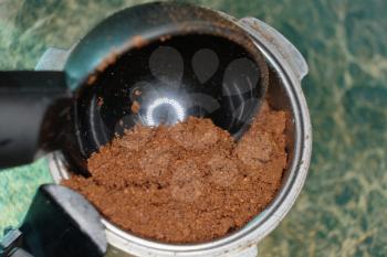 Adding Ground coffee in portafilter with plastic spoon macro image on green surface