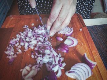 Woman is Cutting shallots with a knife on a wooden cutting board.