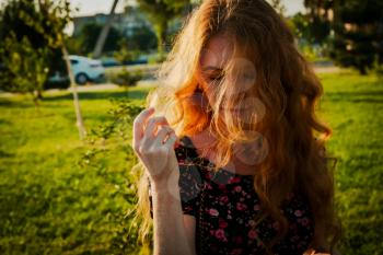 Thoughtful redhead lady wind swept hair covering her face with closed eyes, backlit by summer sun. Summertime alone mood.