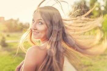 Jollyful lady looking back with her long blond hair fly in an air and lit by warm summer sun.