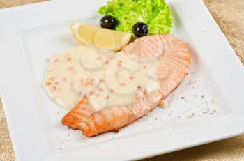 Grilled salmon steak with sauce of cheese and caviar, greens, lemon and olive