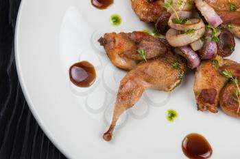 Roasted quails with vegetable on white plate