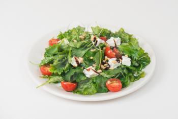 Green salad with vegetables: greens, arugula, tomato, cheese pine nuts and sauce