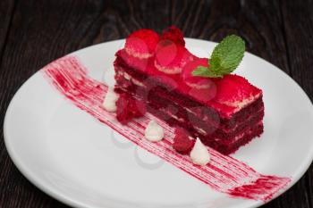 Plate with piece of delicious red velvet cake on dark wooden background