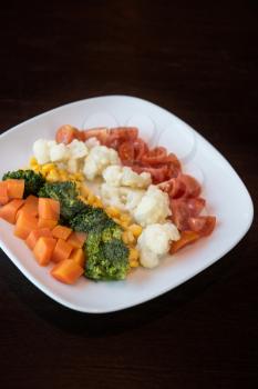 Boiled carrot broccoli corn cauliflower tomato on white plate. Concept. Healthy food. Low-Carb Diet. Vegetarian food.