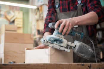 Worker grinds the wood box of angular grinding machine