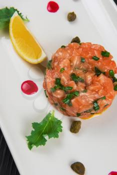 Fresh salmon tartare with lime and capers on white plate