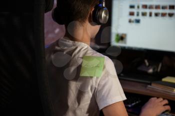 Pasting aprils fools day sticker on young boy shoulder while busy on PC work - concept of April fool day celebration