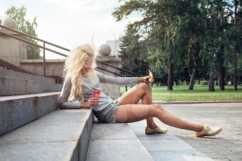 Rest in street, outdoor, people and leisure concept - beauty blonde young woman sitting on outdoor and eating