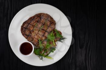 Grilled black angus steak ribeye on white plate on black wooden background