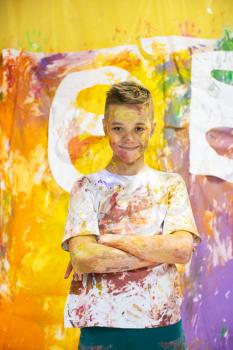 Portrait of a cute happy boy painting and having fun. He is showing his hands face and clothes painted in bright colors