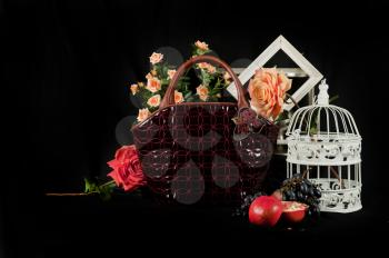 Fashionable handbag  with cage fruits and flowers on black background. 