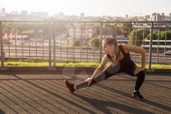 A woman in sportswear doing fitness exercises. City in sunny evening.