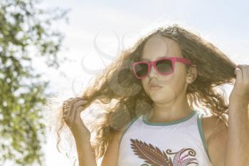 Young girl in sunglasses fixing her long blond hair in the sunlight on a hot afternoon.