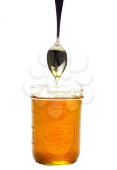 Honey flowing from spoon into a jar isolated over white