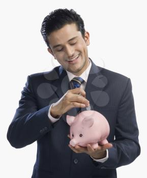 Businessman putting a coin into a piggy bank