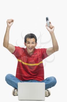 Man cheering in front of a laptop and holding a mobile phone