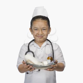 Girl dressed as a nurse and holding a tray of medicines and smiling