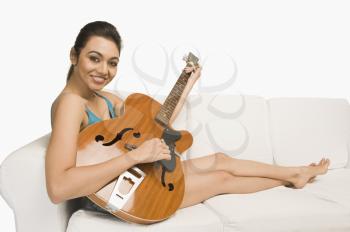 Portrait of a woman sitting on a couch and playing a guitar