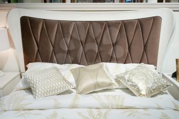 Bed with a big brown soft headboard and pillows.
