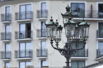 Beautiful classic iron lamppost of six lamps with diode bulbs on the background of a building with windows