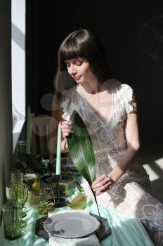 Young girl with an aspidistra leaf next to a window and harsh sunlight.