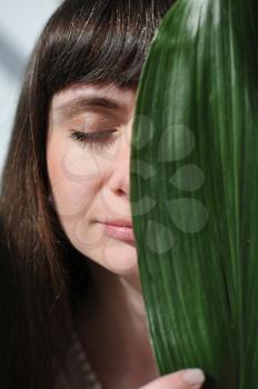 Portrait of a young girl, face close up and half covered by a large sheet of aspidistra