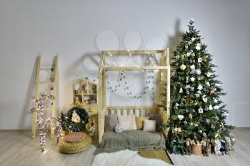 Beautiful children's playroom with wooden furniture, a house and a staircase, decorated for the New Year holiday with a Christmas tree and a deer from a garland