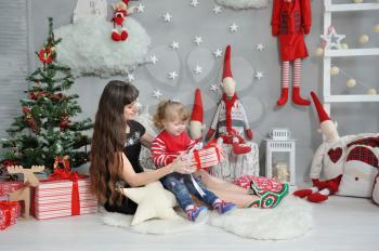 Brunette Mom gives a present to her lovely daughter on the background of Christmas decor with gnomes and garlands