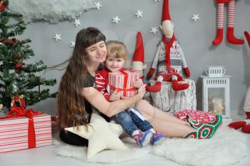 Happy brunette mom hugs her cute daughter on a background of Christmas decor with gnomes and garlands