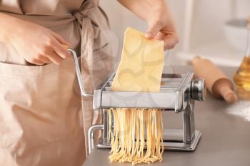 Woman making noodles with pasta machine at table�