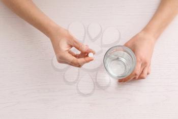 Young woman taking pill at table, top view�