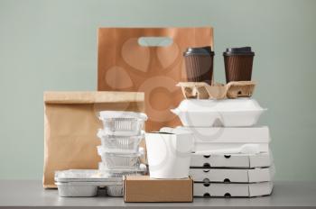 Different packages and carton cups on table against color background. Food delivery service�