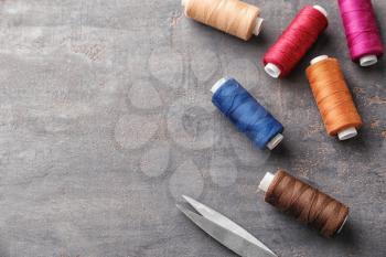 Sewing threads and scissors on grey background�