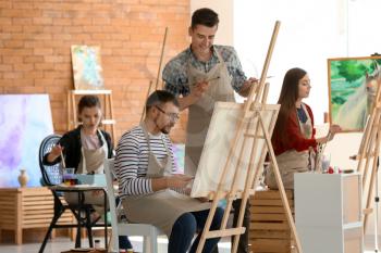 Male teacher helping his student during classes in school of painters�