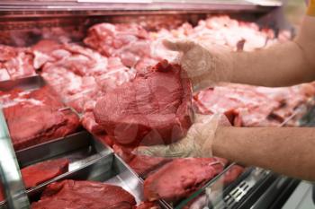 Male seller holding piece of fresh meat in butcher shop�