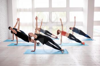 Group of sporty people practicing yoga indoors�