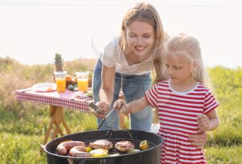 Young woman with daughter cooking meat, sausages and vegetables on barbecue grill outdoors�