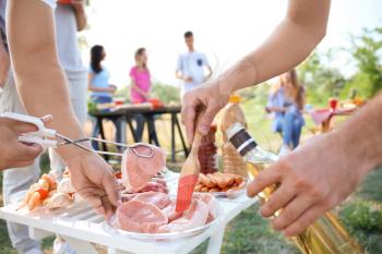 Young people preparing meat for barbecue party outdoors�