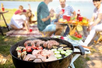 Meat and vegetables on modern barbecue grill with group of friends outdoors�