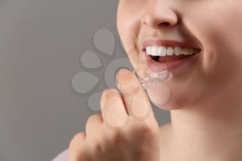Woman putting occlusal splint in mouth on grey background, closeup�