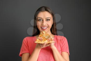Young woman eating slice of hot tasty pizza on color background�